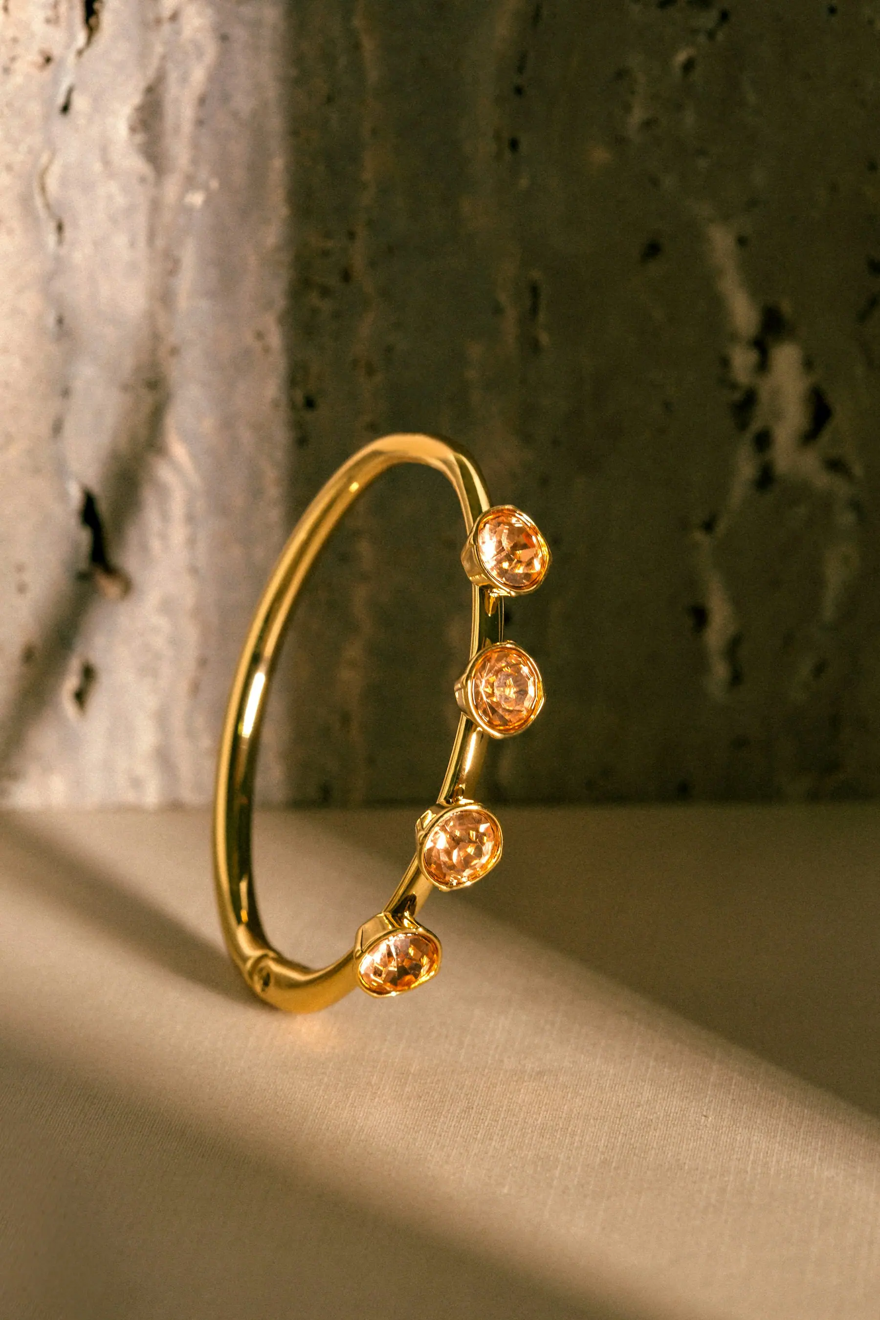 A warm gold bangle set with pale stones, photographed against dark wood