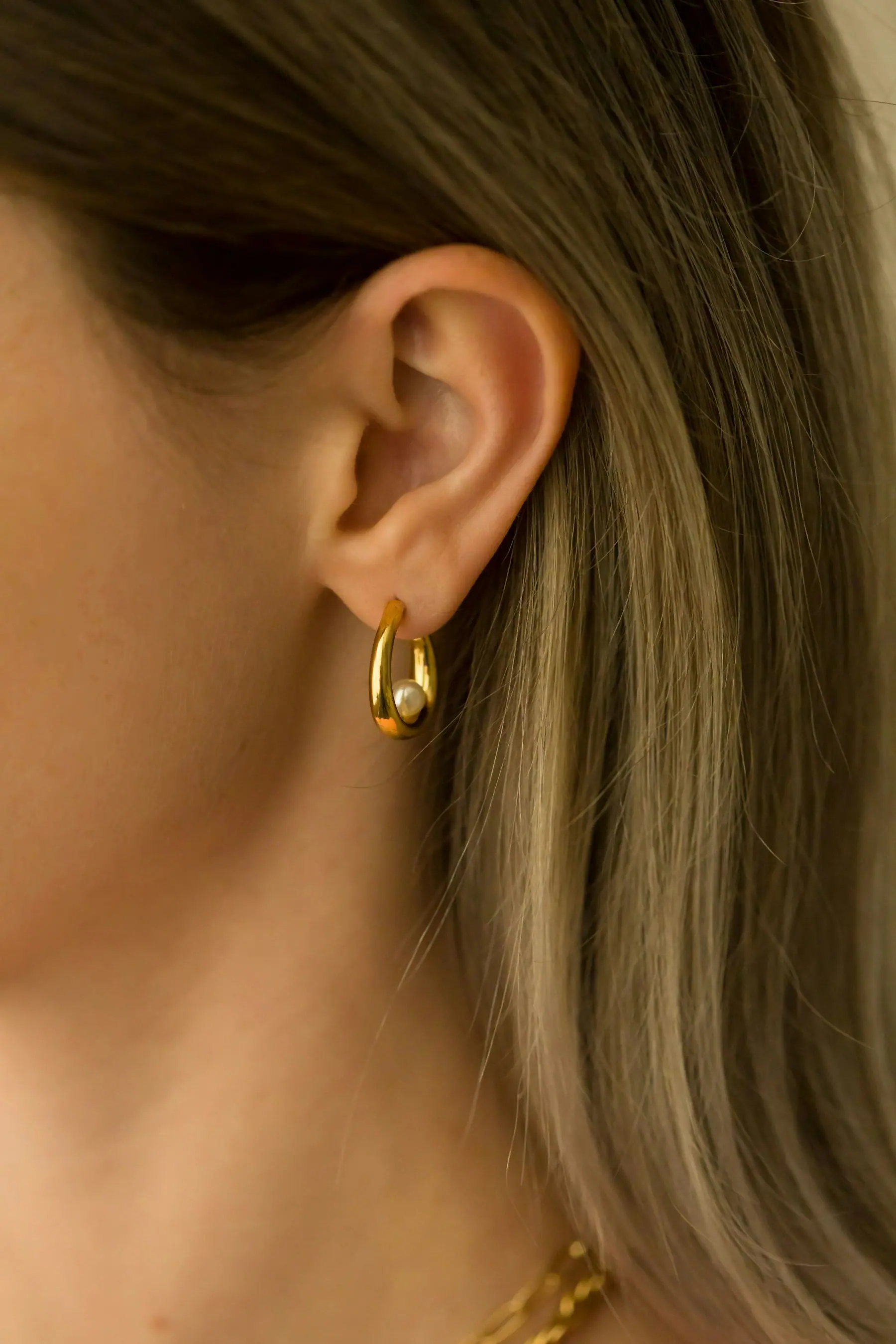 A small rolled gold huggie earring worn on the lobe