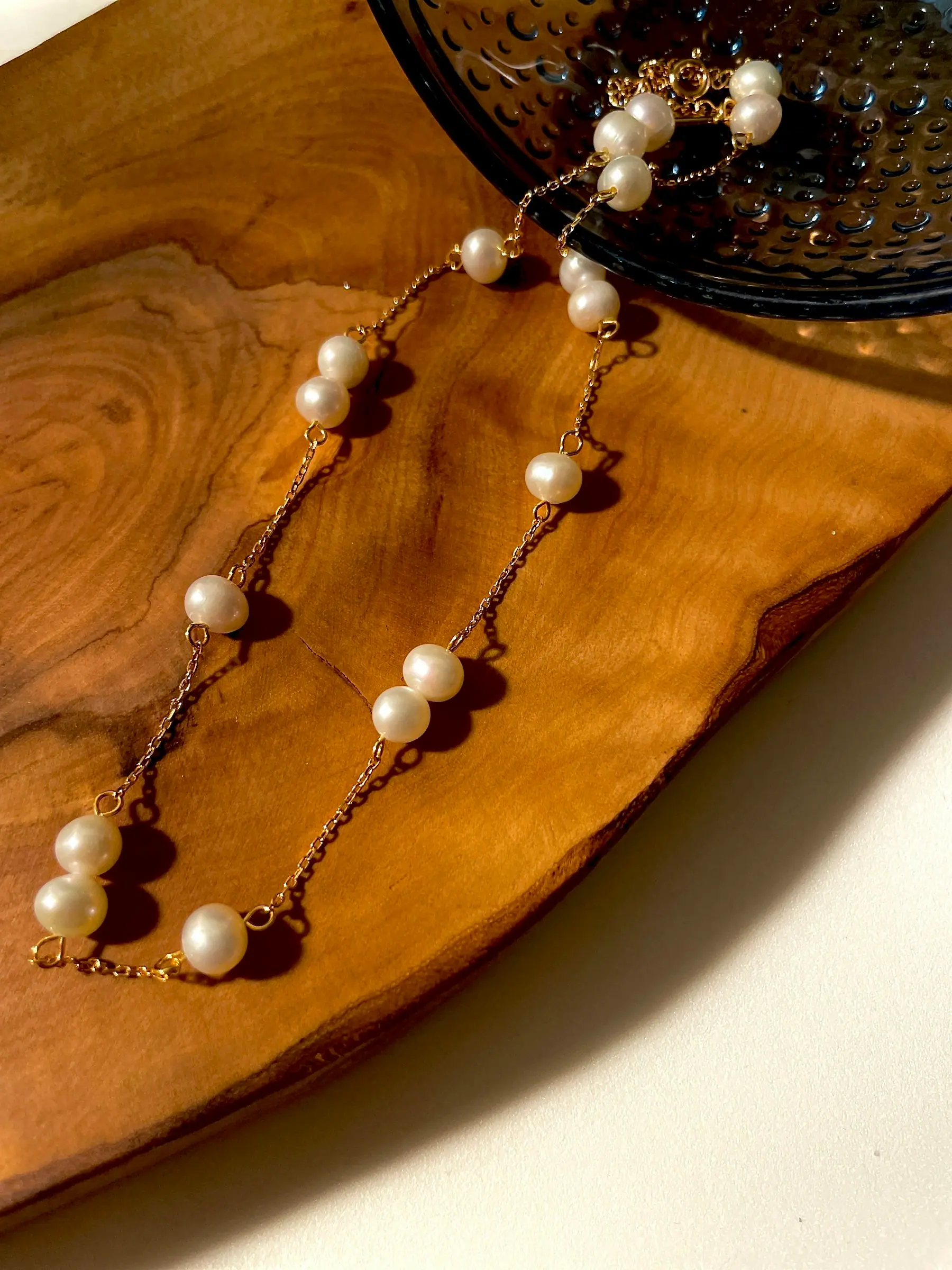 A pearl and rolled gold chain laid across a wooden board