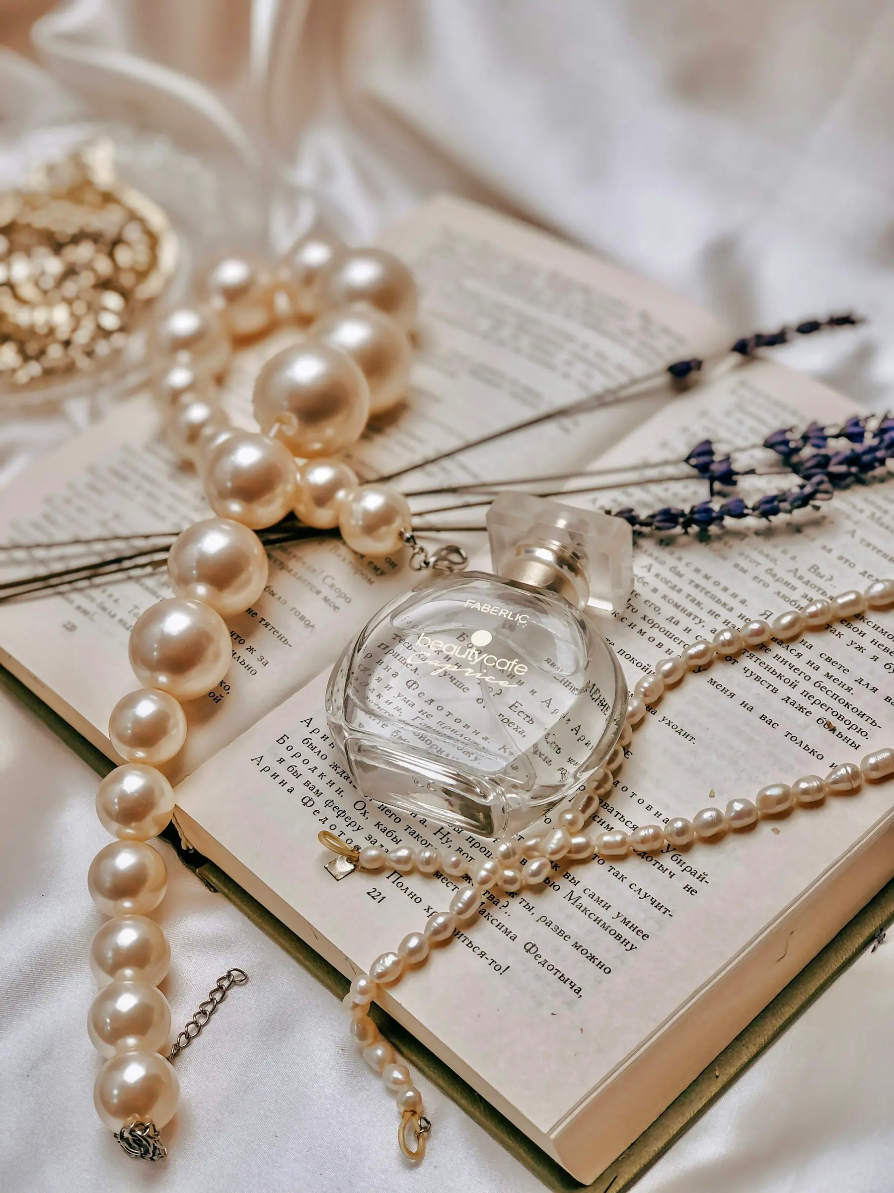 Pearls and a fine chain arranged on an open book beside a glass bottle